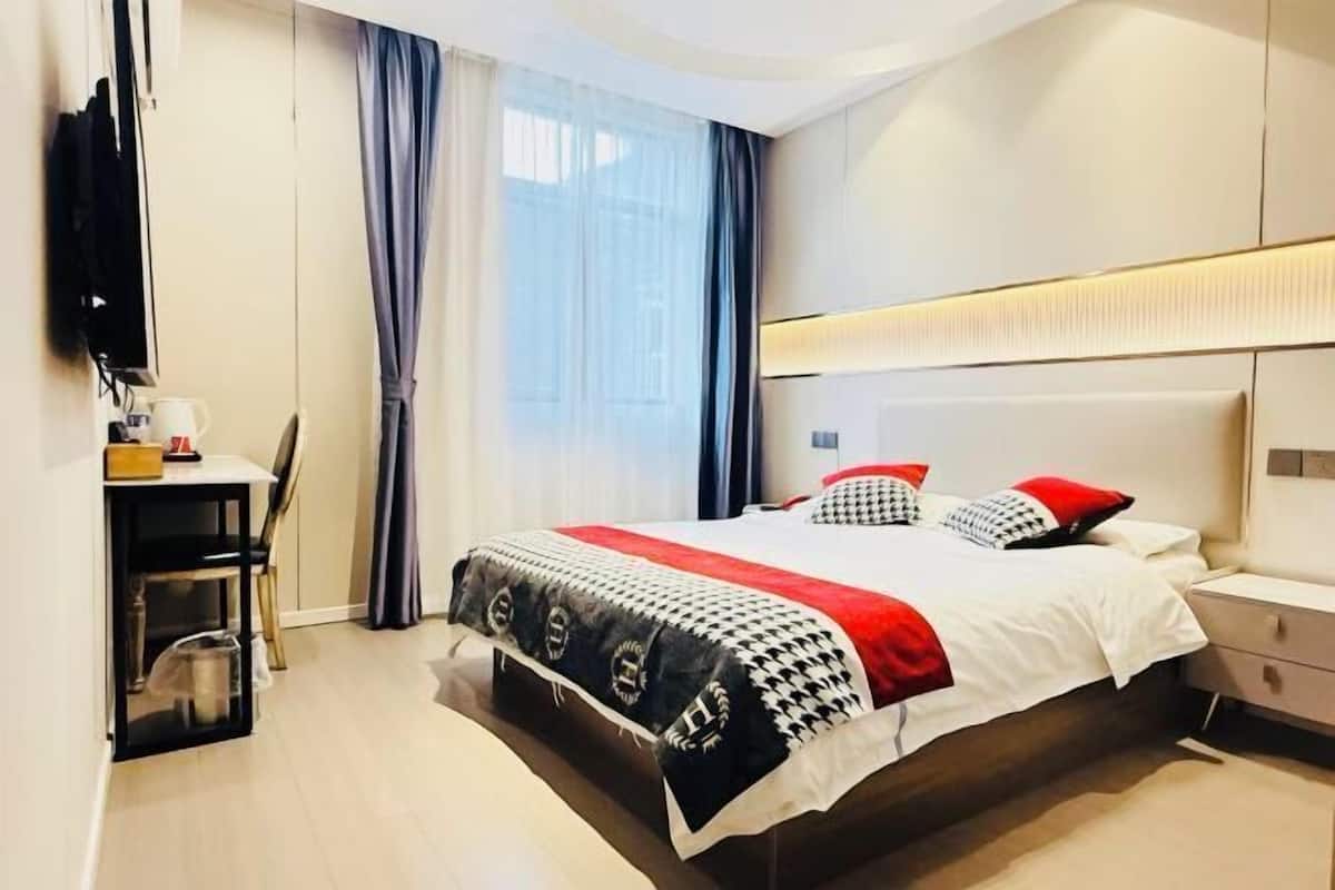 A modern hotel room with a large bed, a desk with a chair, a TV, and a window with curtains.