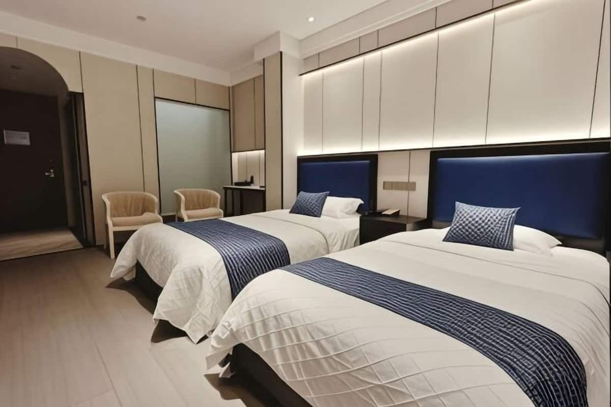 A hotel room with two beds, a sitting area, and a large mirror.