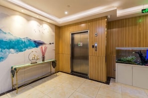 A hotel lobby with a wooden panel wall, a glass-topped reception desk, an elevator, and a fish tank. - Longchen Holiday Inn (Shanghai Ruijin Hospital Yongjia Road Branch) (Shanghai)