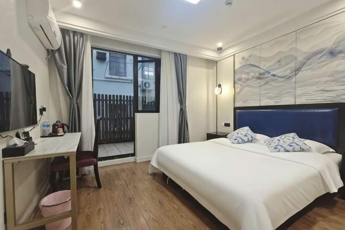 A bedroom with a bed, a desk, a chair, a TV, and a window with curtains.
