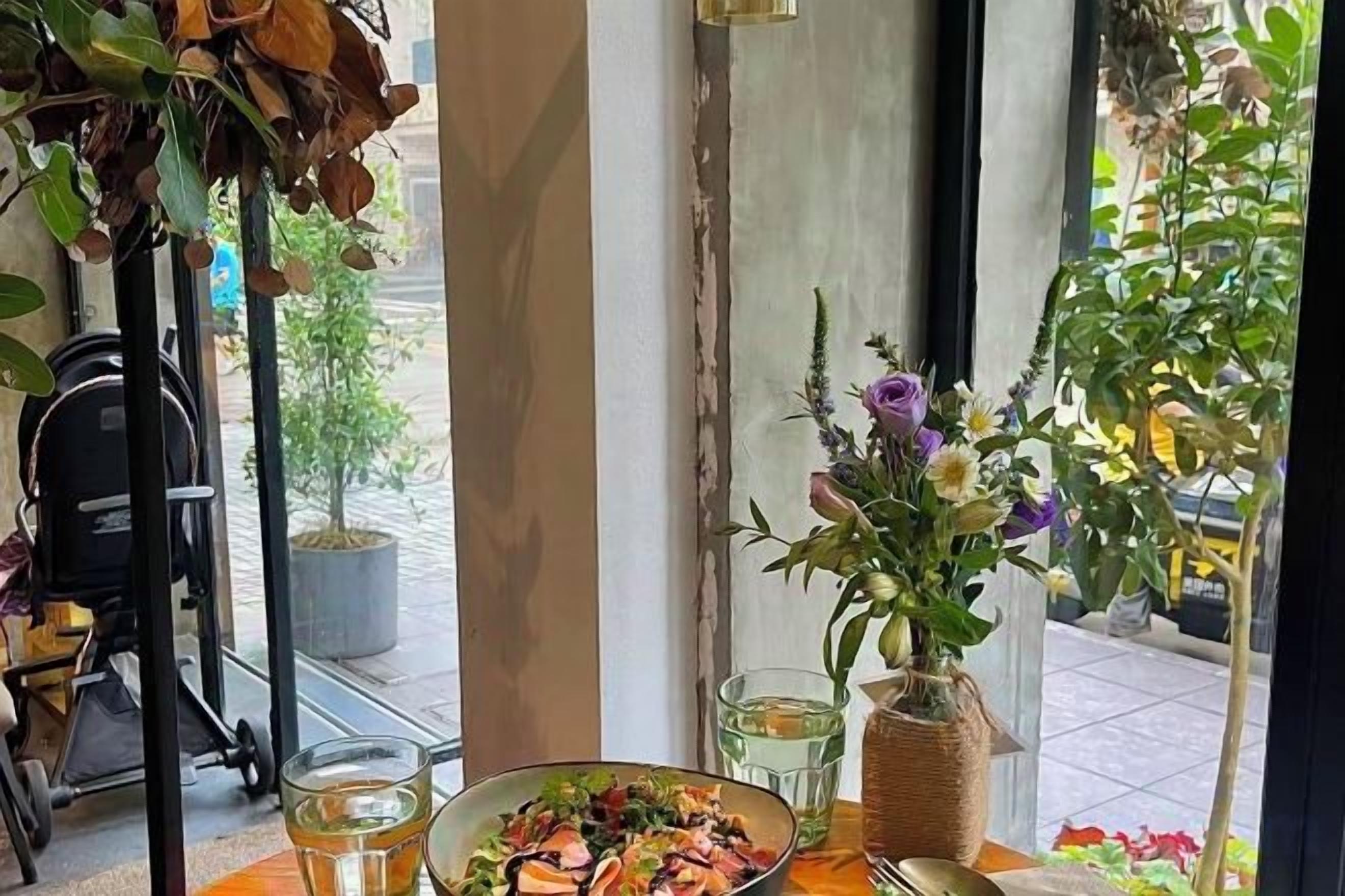 A dining table with a salad, a vase of flowers, and a glass of water.