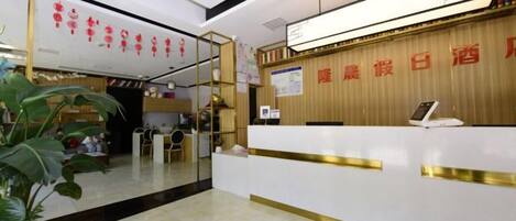 A hotel reception area with a reception desk, a digital screen, and a wooden wall with red text.