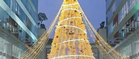 A large, illuminated Christmas tree in an urban setting with modern buildings in the background.