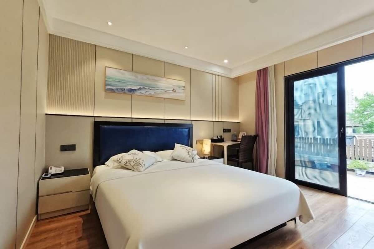 A modern hotel room with a large bed, a nightstand, a desk, and a view through a glass door.
