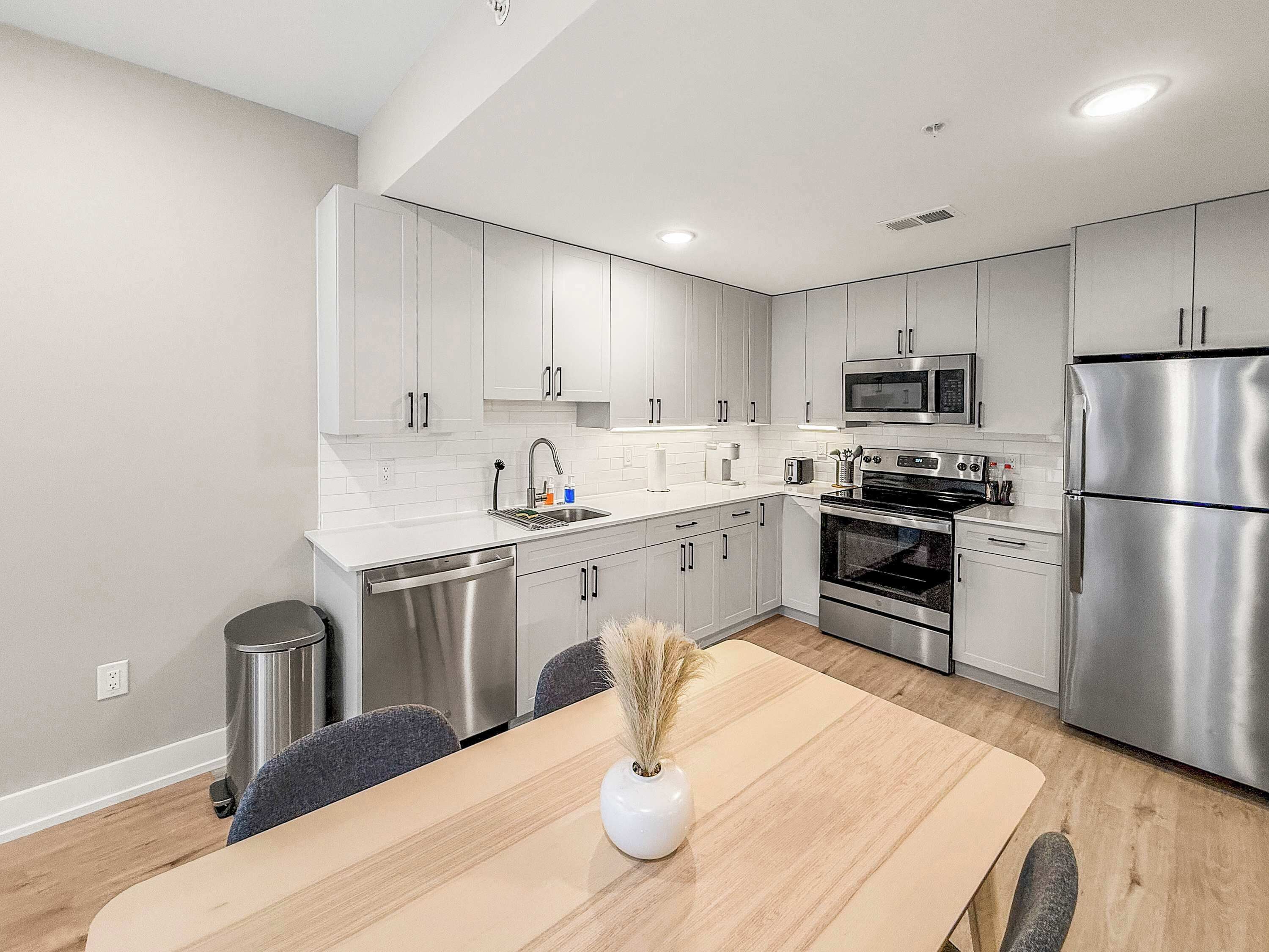 Una cocina moderna con electrodomésticos de acero inoxidable, armarios blancos y un comedor con mesa y sillas de madera.