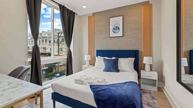A hotel room with a large bed, bedside tables, a desk, and a window with curtains.