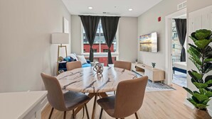 A modern dining area with a marble table and chairs, a sofa, a lamp, and a view of a building outside.