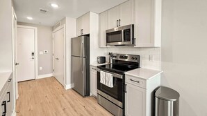 A modern kitchen with stainless steel appliances, white cabinetry, and a wooden floor. - Luxury Studio | 1 Bed | Northern Liberties (Philadelphia)