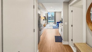 Een moderne hal met een houten vloer, een keuken met een koelkast, en een eethoek met een blauwe bank.
