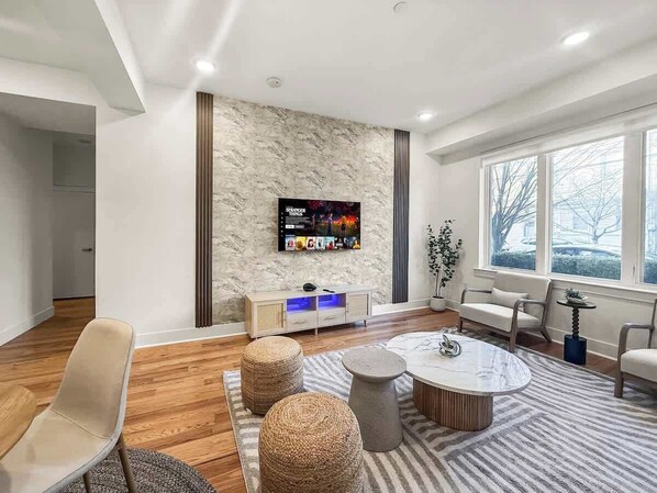 A modern living room with a flat-screen TV, a sofa, a coffee table, and a large window with a view.