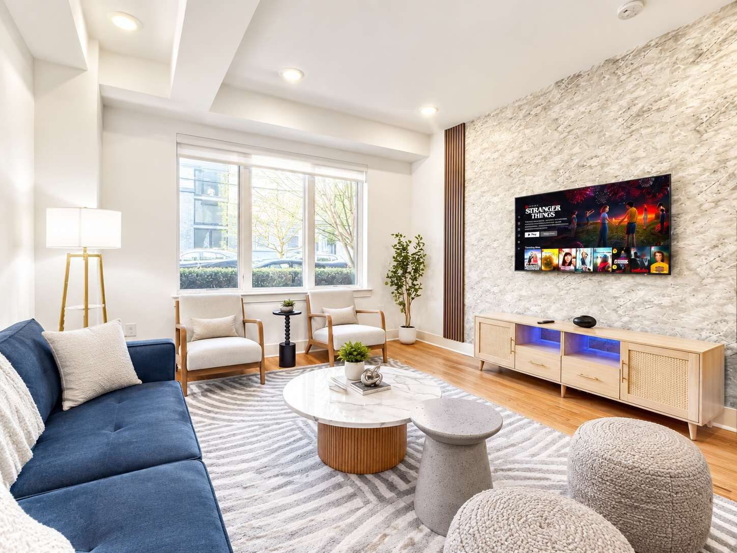 Een moderne woonkamer met een bank, stoelen, een salontafel en een televisie bevestigd aan een gestructureerde muur.