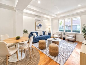 A modern living room with a blue sofa, round coffee table, and a dining table with chairs.