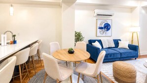 A modern living room with a round wooden table, white chairs, a blue sofa, and a small plant.