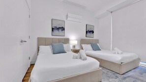 Hotellihuone, jossa on kaksi sänkyä, yöpöytä lampun kanssa ja taideteoksia seinällä.
