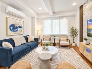 A modern living room with a blue sofa, round coffee table, and a large window with natural light.