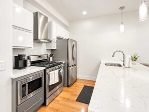 A modern kitchen with stainless steel appliances, a marble countertop, and a black rug. - Modern Philly Haven | 1BD | Northern Liberties (Philadelphia)