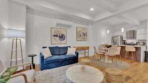 Un soggiorno moderno con un divano blu, un tavolino da caffè in marmo rotondo e un'area pranzo con tavolo e sedie in legno.