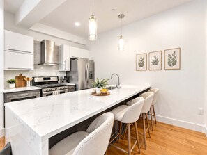 A modern kitchen with stainless steel appliances, a marble countertop, and a bar area with stools. - Modern Philly Haven | 1BD | Sleeps 4 | Northern Liberties (Philadelphia)