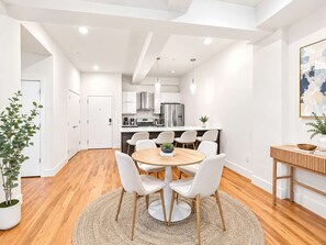 A modern kitchen with white cabinets, stainless steel appliances, and a dining area with a round table and white chairs.