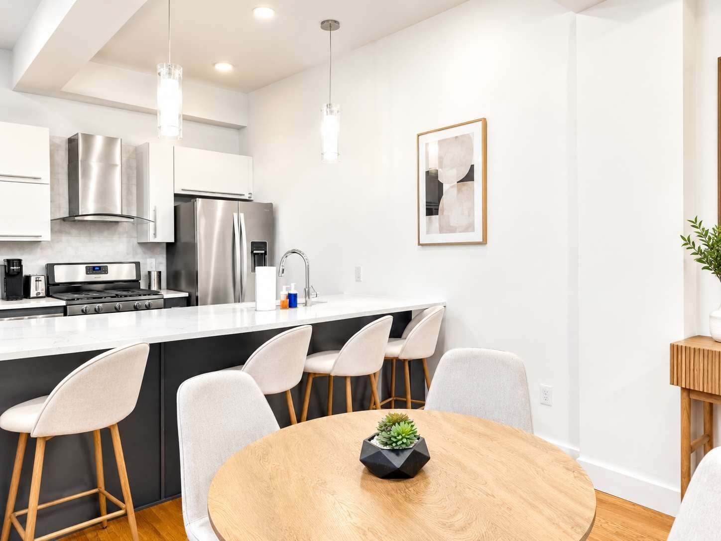A modern kitchen with stainless steel appliances, a central island with bar stools, and a dining table with a potted plant.
