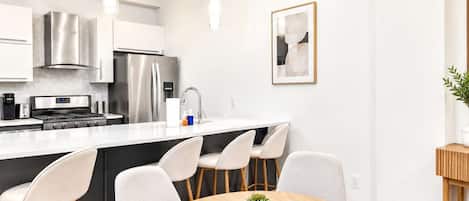 A modern kitchen with stainless steel appliances, a central island with bar stools, and a dining table with a potted plant.