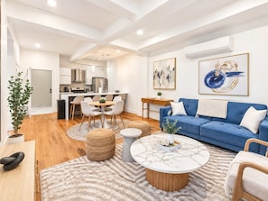 Una sala de estar moderna con un sofá azul, una mesa de centro redonda y un comedor con una mesa y sillas blancas.