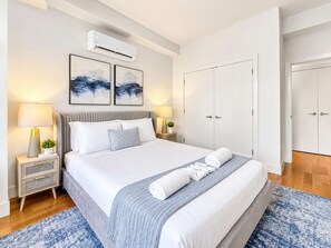 A modern bedroom with a bed, nightstands, an air conditioning unit, and a wardrobe. - Modern Philly Haven | 1BD | Northern Liberties (Philadelphia)