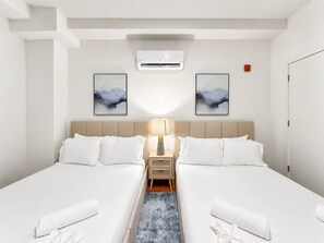 A hotel room with two beds, a nightstand, a lamp, and two abstract paintings on the wall.