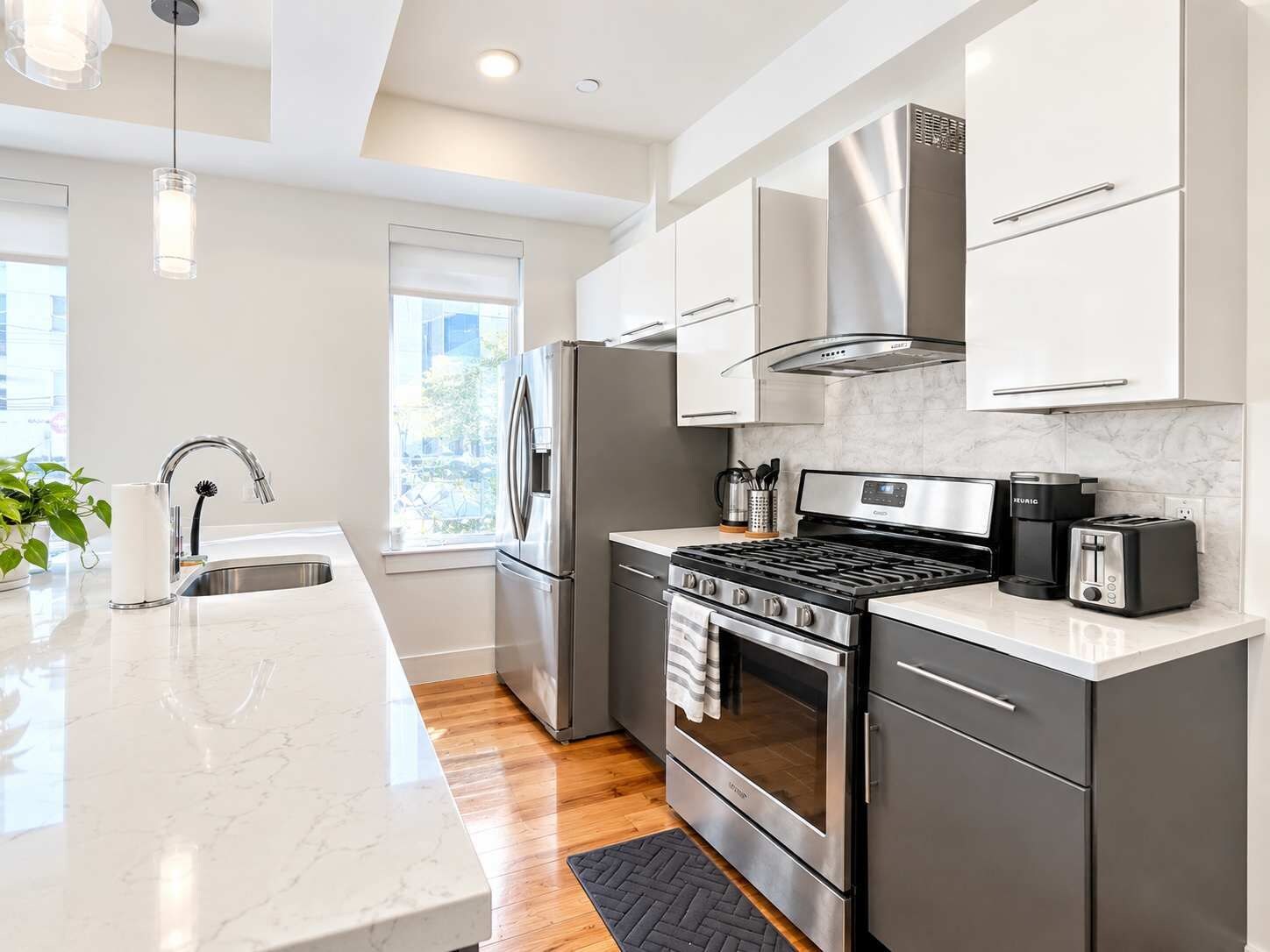 A modern kitchen with stainless steel appliances, a marble countertop, and a window providing natural light.