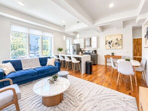 A modern living room with a blue sofa, a coffee table, and a dining area with chairs. - Cozy Luxury 2BD | Sleeps 8 | Northern Liberties (Philadelphia)