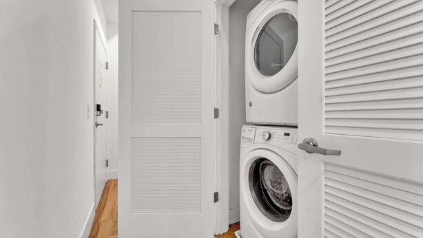 A laundry room with a front-loading washer and dryer, a closed door, and a wooden floor.