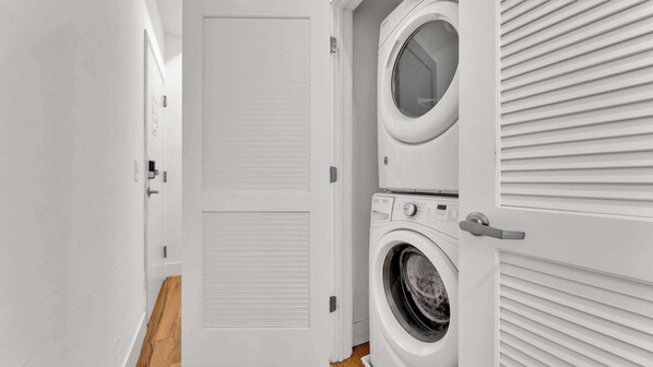 A laundry room with a front-loading washer and dryer, a closed door, and a wooden floor.