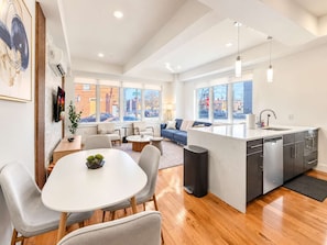A modern kitchen with a central island, dining area with chairs, and a living room with a sofa and coffee table.