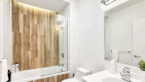 A modern bathroom with a glass shower enclosure, white tiles, and a wooden accent wall.
