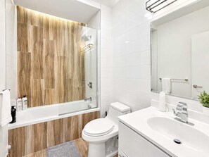 A modern bathroom with a glass shower enclosure, white tiles, and a wooden accent wall.