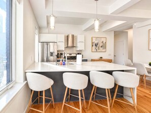 A modern kitchen with a central island, bar stools, stainless steel appliances, and pendant lighting. - Cozy Luxury 2BD | Sleeps 8 | Northern Liberties (Philadelphia)