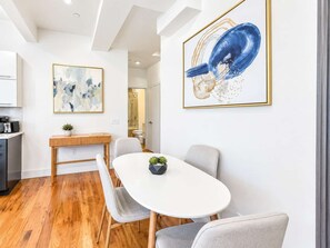 A modern dining area with a white table, grey chairs, and wooden flooring. There are two framed artworks on the walls.