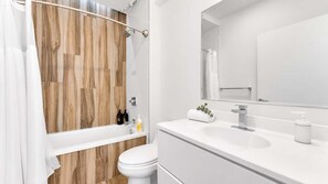 A modern bathroom with a wooden wall, a white bathtub, a toilet, and a sink with a mirror.