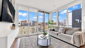 A modern living room with a sofa, coffee table, and large windows offering a city view.