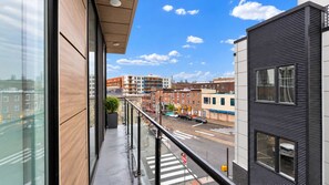 Un balcon donnant sur une rue de la ville, des immeubles et un ciel dégagé.