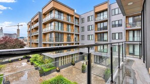 Un immeuble résidentiel à plusieurs étages, doté de balcons, d’une cour intérieure agrémentée de verdure et, au loin, d’une grue de construction.