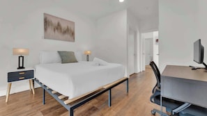 Une chambre à coucher moderne, avec un lit, des tables de chevet, un bureau avec une chaise et un tableau accroché au mur.