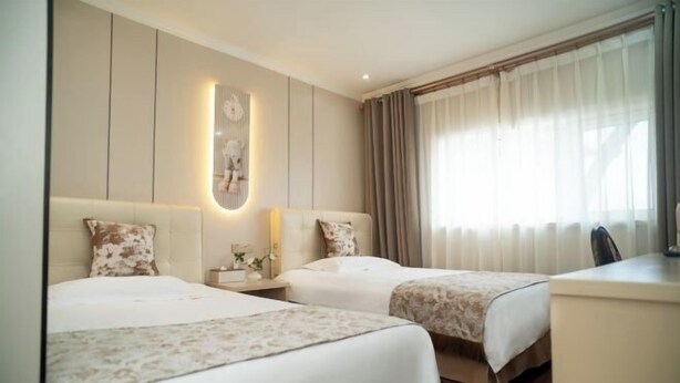 A hotel room with two beds, a desk, a chair, a nightstand with a lamp, and a large window with curtains. - Qingxu Jinrui 99 Boutique Hotel (Qingxu)