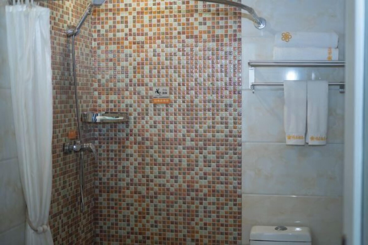 A bathroom with mosaic tile walls, a shower, a toilet, and a towel rack.