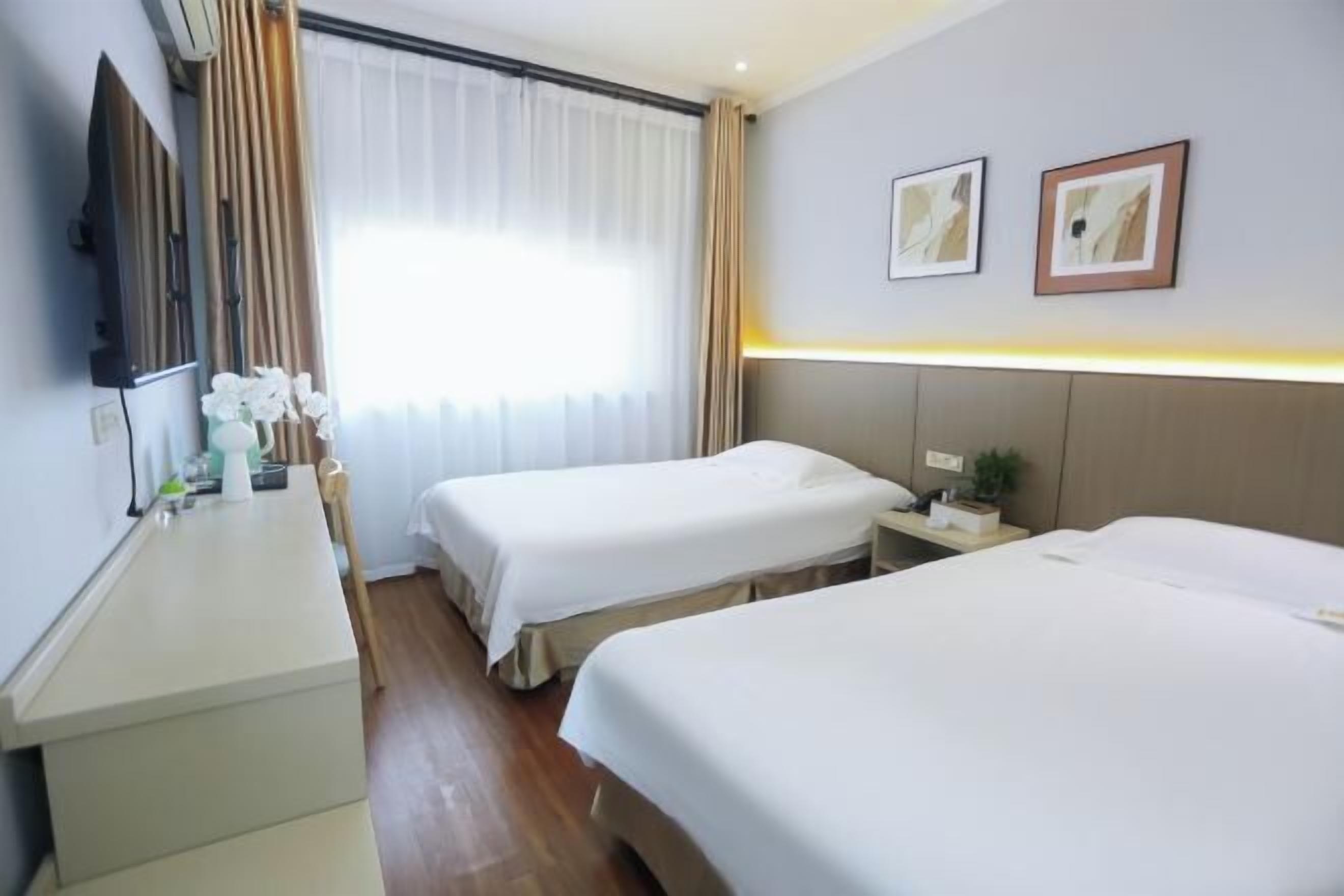 A hotel room with two beds, a bedside table, a TV, and a window with curtains.