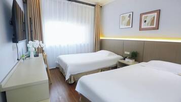 Quarto de hotel com duas camas, uma mesinha de cabeceira, televisão e janela com cortinas.
