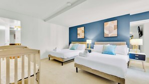 A hotel room with two beds, a crib, a bathroom with a mirror, and artwork on the walls.