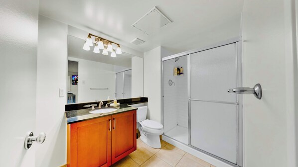 A bathroom with a white sink, wooden cabinets, a toilet, and a glass-enclosed shower.