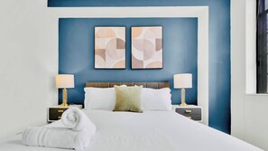 A hotel room with a large bed, two bedside tables, and abstract wall art. - Modern 2BD | Center City | 4 Beds | Near JFK Plaza (Philadelphia)