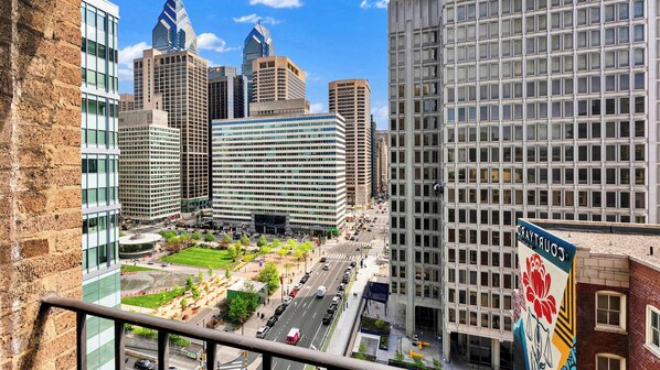 A cityscape with modern high-rise buildings, a central green space, and a street with vehicles.